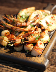 Fried prawns shrimps, squid and scallops with herbs, pepper and spices on wooden board.  Summer picnic, sunny day. Background image, copy space