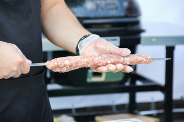 The process of cooking, preparation. Raw lula kebab on a skewer with the hands of a cook. Summer picnic grill. Background image, copy space