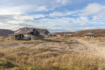 Russia, Arctic, Kola Peninsula, Barents Sea, Teriberka: Run down abandoned wooden house in the city center of the old Russian settlement small fishing village with green grass and grey cloudy sky