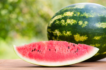Single slice of ripe red juicy watermelon on a wooden table in the garden in summer time