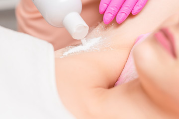 Cosmetologist hand is sprinkling talcum powder on armpit of young woman before the depilation procedure. Epilation and sugaring of armpit.