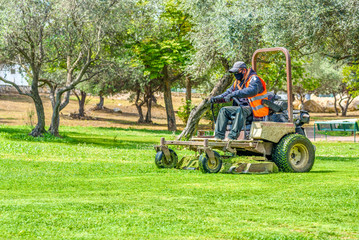 Man wear safety masks as a precaution after outbreak the Covid 2019 during mows the grass with lawn mower.