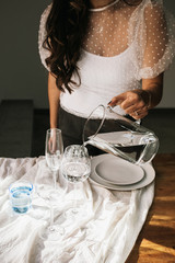 Hands with jug of water and glasses on wooden table