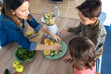 Two boys helping his mother to prepare a detox juice with blender in the kitchen at home.