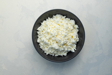A close-up of rustic cottage cheese in a black ceramic bowl. Horizontal orientation, selective focus, view from above.