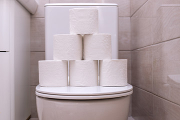 rolls of white toilet paper are piled on the toilet lid in the bathroom