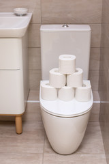 rolls of white toilet paper are piled on the toilet lid in the bathroom