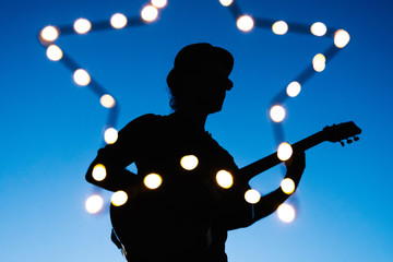 Detail of shape of man playing the guitar on a night live concert. Acoustic music festival at spring and summer nights. Music star performing with a guitar at sunset.