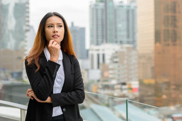 Young beautiful Asian businesswoman thinking against view of the city