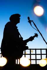 Music star performing with a guitar at sunset. Man singing on a night live concert with microphone....