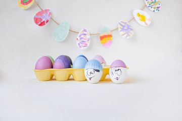 On a yellow stand are painted eggs on a white background. Real hand-painted eggs. A multi-faceted photo. The white photo has funny cute faces on the eggs. Holiday and joy of Bright Easter