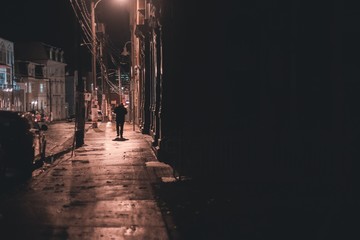 shadowy figure walking down wet street at night st. johns, newfoundland, canada
