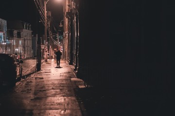 shadowy figure walking down wet street at night st. johns, newfoundland, canada © Erik