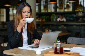 Young beautiful Asian businesswoman drinking coffee at the coffee shop