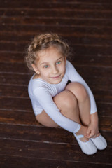 Naklejka premium A charming little girl in a white gymnastic costume is training in rhythmic gymnastics. A little girl is doing exercises on the floor. For a child, the concept