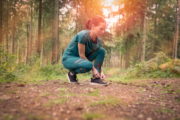 Naklejka na ściany i meble Sporty woman tying up her shoelace before exercise, woodland setting.