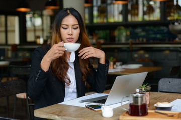 Young beautiful Asian businesswoman drinking coffee at the coffee shop