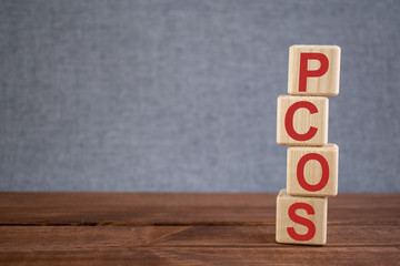 Abbreviation PCOS (polycystic ovarian syndrome) text acronym on wooden cubes on dark wooden backround. Medicine concept.