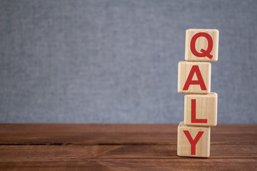 Abbreviation QALY (Quality adjusted life year) text acronym on wooden cubes on dark wooden backround. Medicine concept.