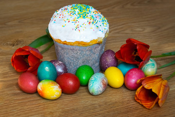 
Easter cake with colored sprinkles and multi-colored bright colored eggs on a wooden background. With red tulips.