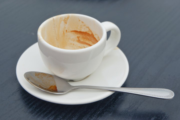 Dirty coffee cup on black wood table in cafe shop.Coffee drink on woode.n table.lose up view of cup of coffee on saucer.Close up.