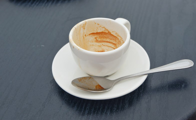 Dirty coffee cup on black wood table in cafe shop.Coffee drink on woode.n table.lose up view of cup of coffee on saucer.Close up.
