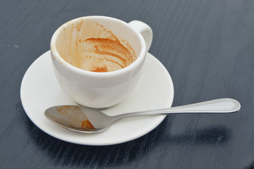 Dirty coffee cup on black wood table in cafe shop.Coffee drink on woode.n table.lose up view of cup of coffee on saucer.Close up.