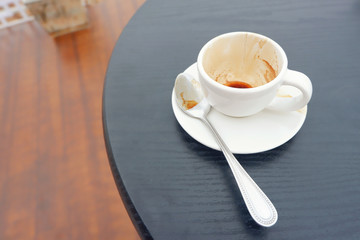 Empty and dirty white tea cup on wood table in cafe.Tea cup with spoon on black wood table,Close up.