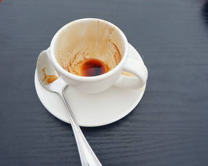 Empty and dirty white tea cup on wood table in cafe.Tea cup with spoon on black wood table,Close up.