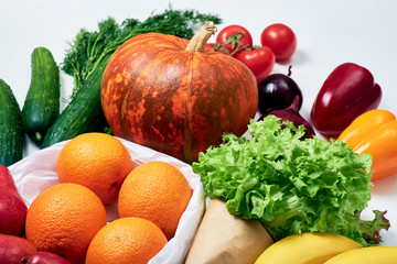 Groceries: pumpkin, sprig of tomatoes, red onions, red and yellow bell peppers, cucumbers, dill, oranges, red pears, lettuce, bunch of bananas on white background
