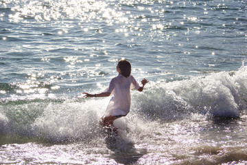 Fototapeta premium Little girl with shirt plays in the waves of the sea