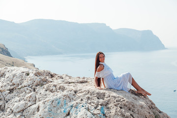 Naklejka na ściany i meble A beautiful woman with long hair in a dress looks at the landscape