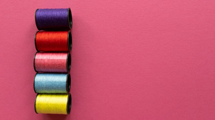 Violet, red, pink, blue, yellow colors spools of threads on pastel texture background. Flat lay with copy space. Stock photo.