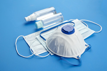 Antibacterial hand sanitizer, respirator and surgical masks on blue background