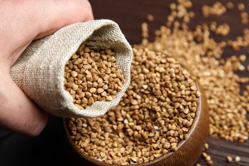 Buckwheat groats (hulled seeds) in bowl and burlap bag on wooden table