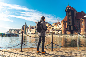 Theme of tourism in Poland. Traveling in Gdansk. A male traveler uses a phone on the embankment of the Motlawa River amid the main attraction, a symbol of the city of Gdansk Gate crane