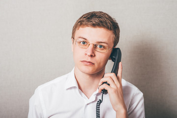 The man in glasses talking on a wired phone. On a gray background.