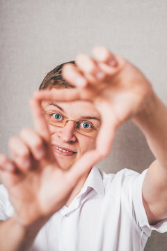 The man in glasses looking through heart his fingers. On a gray background.