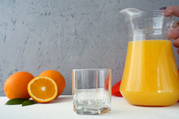 Empty glass and hand of woman holding decanter with orange juice. Oranges on the table