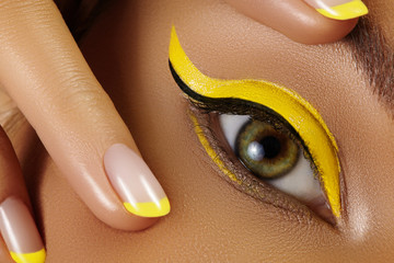 Close-up Female Eye with bright yellow Eyeliner Makeup. Neon Disco make-up and Fashion Manicure....