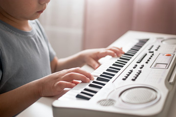 Fototapeta na wymiar Close up child plays a piano keyboard. Boy learns to play the synthesizer