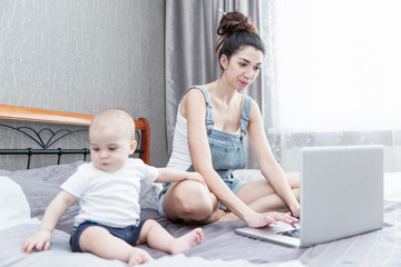 Working at home mom with baby are sitting on the bed. Internet and remote work.