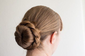 Caucasian young woman with her hair in a french bun with frizzy loose hairs seen from behind not...