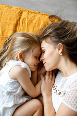 Fototapeta na wymiar Large portrait of mother and daughter. Happy mother and daughter are resting at home on the bed. Yellow bedding. Home comfort