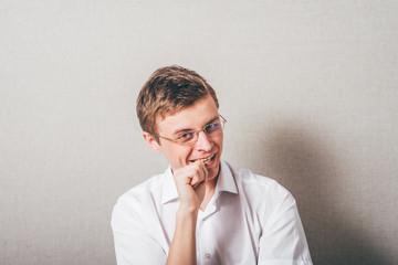 The man with glasses biting his fists, bites his nails. On a gray background.