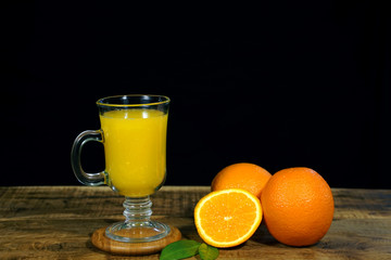 glass of fresh orange juice with fresh fruits on wooden table. black background