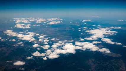 Fototapeta na wymiar Aerial view of mountains under the clouds and blue sky. View from a plane window. Beautiful landscape