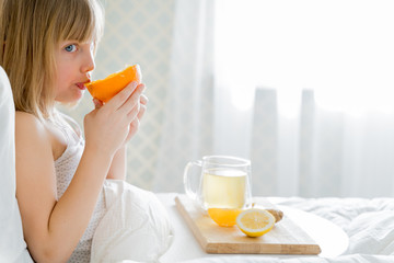 Sick girl in bed tastes half of orange.Cup of antipyretic drugs. Colds,flu.Tea with citrus vitamin C,ginger root,lemon.Wooden tray.Home self-treatment.Medical quarantine therapy. Covid-19,coronavirus