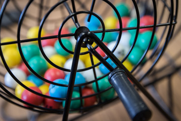 A close up of a bingo cage filled with multi-colored balls. Each ball has a letter and number on it that corresponds to a number on the player's bingo card. Bingo is a game of chance.