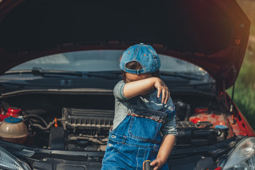 Little child trying to fix broken real car. Dreaming to be auto technician